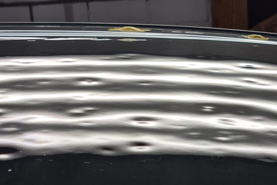 Große Hagel Dellen auf dem Autodach, sichtbar mit der LED-Streifenlampe, Oberfläche wellenförmige Reflektionen und glänzender Textur.
