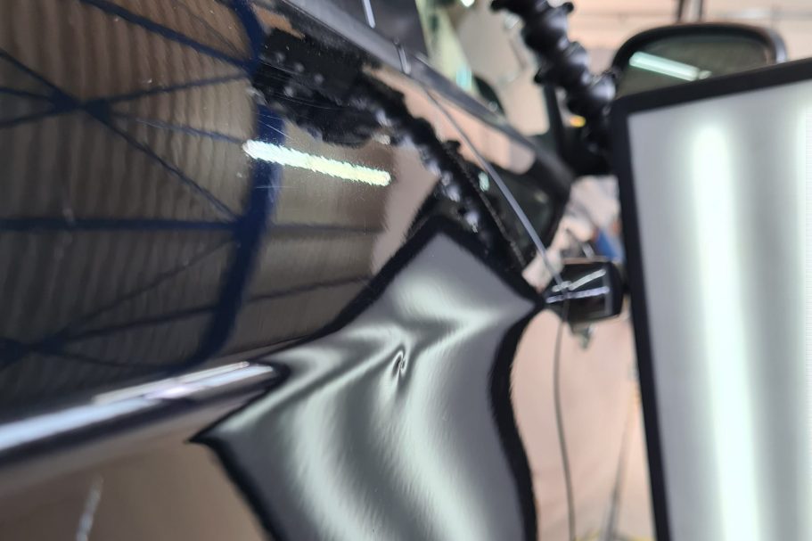 Eine Delle an einer schwarzen Autotür, direkt auf der Designkante, sichtbare Delle mittels einer Reflektion LED-Streifenlampe.